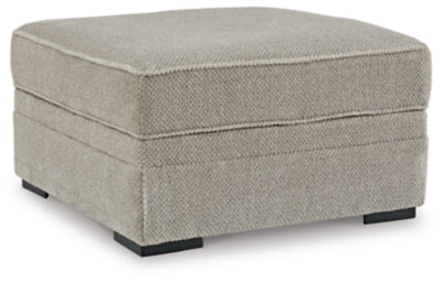 Ashley Furniture Calnita Ottoman with storage, beige fabric, sturdy wooden legs, and a cushioned top, shown from a side angle.