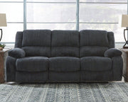 Ashley Furniture Draycoll reclining sofa with plush upholstery and padded armrests, shown in a modern living room setting.