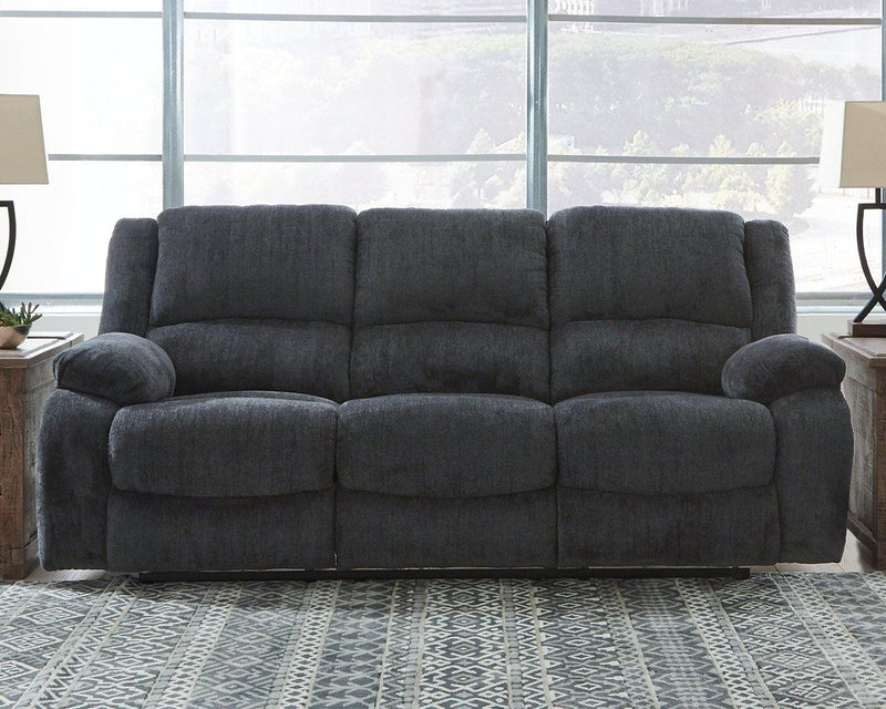 Ashley Furniture Draycoll reclining sofa with plush upholstery and padded armrests, shown in a modern living room setting.