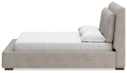 Ashley Furniture Cabalynn upholstered bed with a padded headboard and neutral fabric, shown from a side angle.